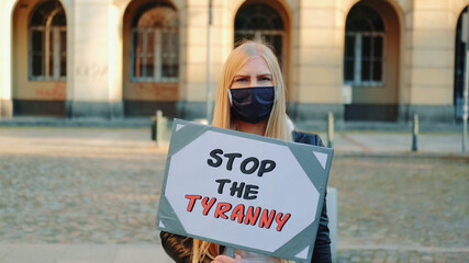 Young woman in protective mask calling to stop the tyranny by holding steamer. Protest walk in the...