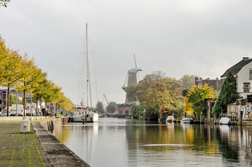 Fototapeta na wymiar Schiedam, the Netherlands, October 23, 2020: a mix of modern and traditional industries around Buitenhaven (outer harbour) with a sailboat and the Nolet windmill