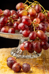 Close-up of wet red grapes in glass fruit bowl, selective focus, on wooden table, vertical black background
