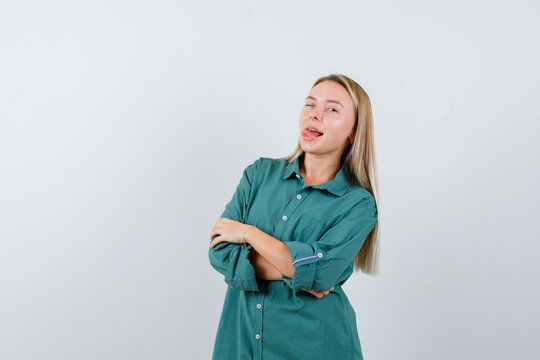  Blonde Girl Standing Arms Crossed, Sticking Tongue Out In Green Blouse And Looking Amused , Front View.