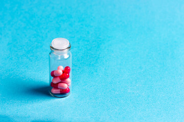 Red-pink pills in a glass jar on a blue background. Pharmaceuticals.