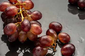 Top view of bunch of wet red grapes on wet slate, selective focus, with back light, horizontal