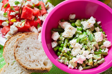 Top view of salad in a pink bowl, watermelon and slices of bread. Selective focus - shallow depth of field.