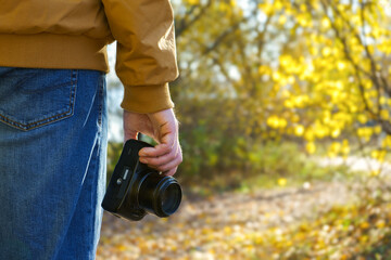Fototapeta premium Closeup of a black camera holding by man's hand with natrural blackground in fall sunny day.