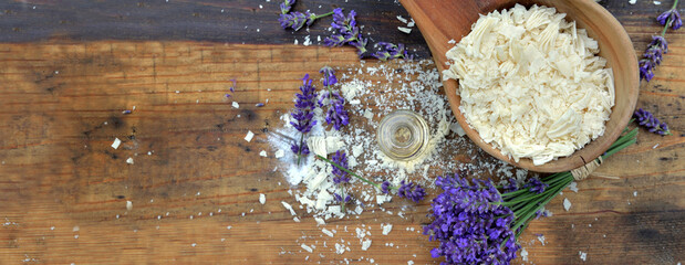 top view on spoon full of flakes of soap with essential oil and lavender flowers on wooden background
