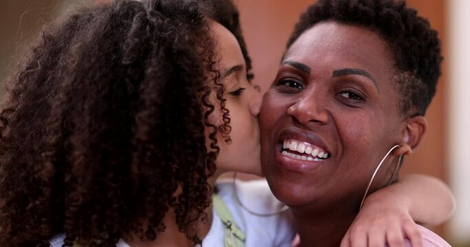 African mother and daughter together. Little girl child kissing mom on cheek, love and affection