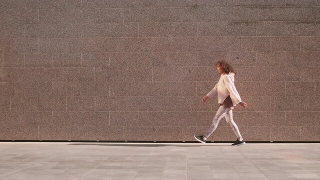 Full stab slow-motion footage of tired fitness woman running along wall taking break breathing while jogging outdoors in summer