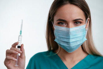 Beautiful female doctor with medical mask. Portrait of nurse with syringe in her hand.