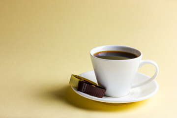 White cup of coffee and chocolates on yellow background