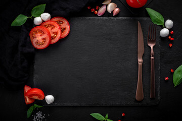 Black slate cooking background with Italian ingredients. Tomatoes, Basil, mozzarella cheese and herbs. concept for a recipe