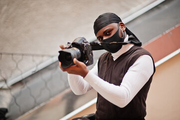Young professional african american videographer holding professional camera with pro equipment. Afro cameraman wearing black duraq and face protect mask, making a videos.