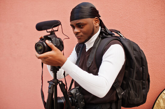 Young professional african american videographer holding professional camera with pro equipment. Afro cameraman wearing black duraq making a videos.