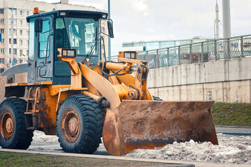 Yellow front loader with snow plow blade removing snow. Snow removal machine for clearing parking lot after winter storm. Loader bucket removing snowdrift. Tractor clean snow, removal road services