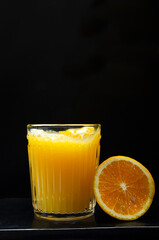Vertical image.Glass full of sweet delicious orange juice and slice of orange against dark background