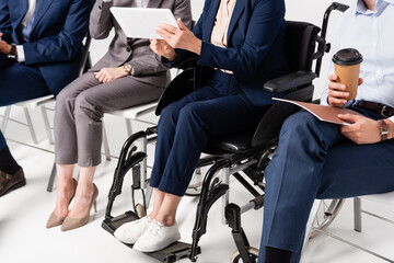 Cropped view of senior businesswoman in wheelchair holding digital tablet near colleagues on...
