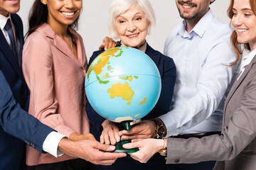 Globe in hands of smiling multiethnic businesspeople on blurred background isolated on grey