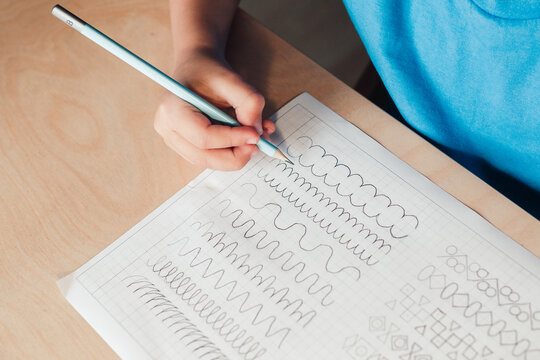 Close up of cute boy doing writing exercises. Child use pencil to draw lines. Children education concept