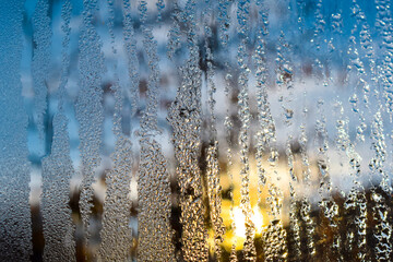 Frozen water drops on the window on a winter morning. The rising sun in the background.