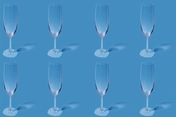 Pattern. Repetition of the image of a champagne glass on a light blue background. Glass wine glasses stand in a row on a light blue surface.