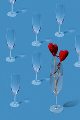 Valentine's day pattern. Copy image of an empty champagne glass on a light blue background. One glass of wine and two red hearts. Vertical.