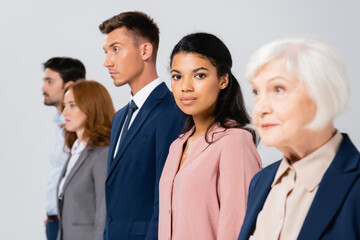 African american businesswoman looking at camera near colleagues on blurred background isolated on grey