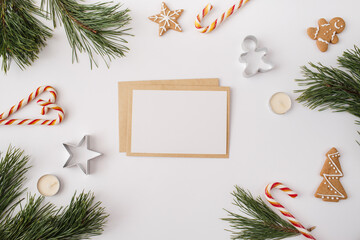 Christmas, New year composition. Paper blank mock up, fir tree branches, candies, gingerbread, candles on white background. Flat lay, top view, copy space