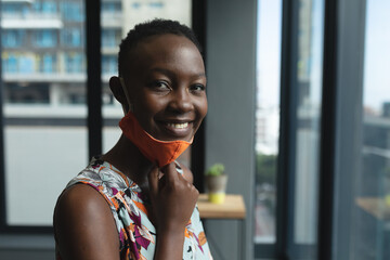 Portrait of african american woman pulling down face mask and smiling in office