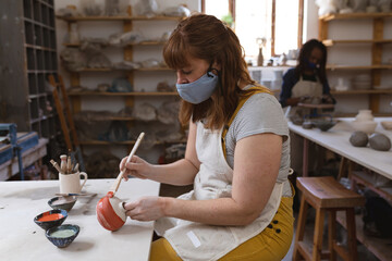Caucasian female potter in face mask working in pottery studio