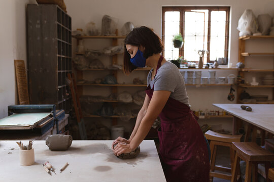 Caucasian female potter in face mask working in pottery studio