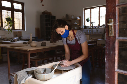 Caucasian female potter in face mask working in pottery studio