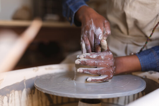 Mixed race female potter in face mask working in pottery studio