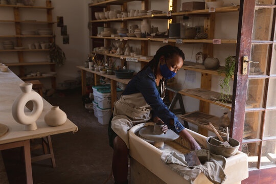 Mixed race female potter in face mask working in pottery studio