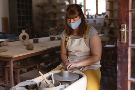 Caucasian female potter in face mask working in pottery studio