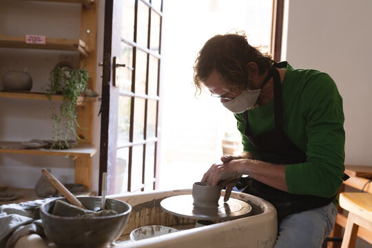 Caucasian male potter in face mask working in pottery studio
