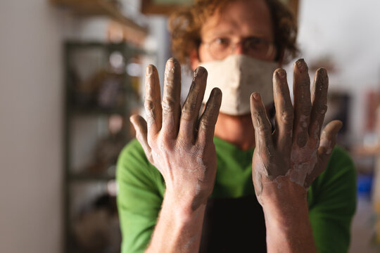 Caucasian male potter in face mask working in pottery studio - Powered by Adobe