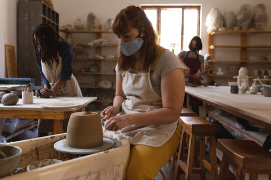 Caucasian female potter in face mask working in pottery studio