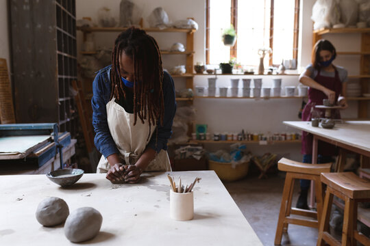 Mixed race female potter in face mask working in pottery studio