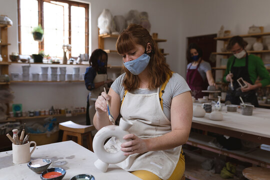 Caucasian female potter in face mask working in pottery studio