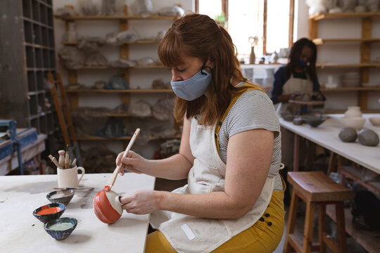 Caucasian female potter in face mask working in pottery studio