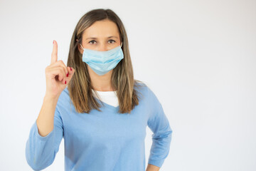 Woman wearing surgical mask pointing up finger over white background.