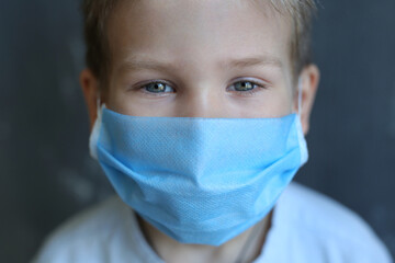  A five-year-old boy wearing a mask and gloves is protected from coronavirus. Blond boy in black medical mask against coronavirus.Boy in black mask on a black isolated background.