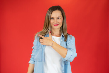 Young woman over isolated red background pointing finger to the side