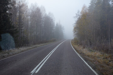 Fototapeta premium Poor visibility. The road is in heavy fog, along the edges of the road there is a forest. Autumn morning in November. Photo through the windshield of a car
