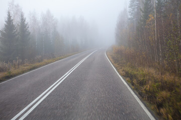 Poor visibility. The road is in heavy fog, along the edges of the road there is a forest. Autumn morning in November. Photo through the windshield of a car