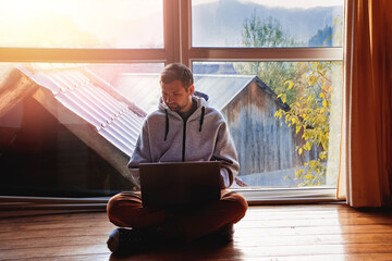 Man using laptop sitting on the floor near big window