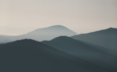 Obraz premium Beautiful, colorful mountain range landscape in soft blue tones with morning fog at sunrise.