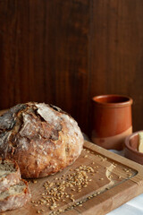 
Round shaped homemade bread is on a wooden board where there are cereals and pottery on a wooden background.
