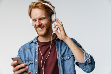 Joyful handsome redhead guy in headphones using cellphone