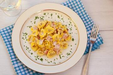 Tortellini with cream and ham on plate served wiyh glass of  wine on white wooden table background.Cooy space