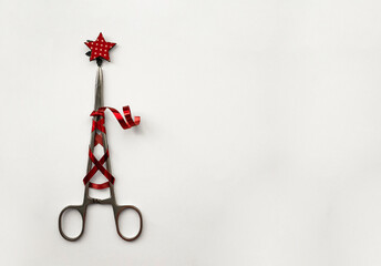 Surgical clip with festive red ribbon and star. Christmas tree made of surgical instruments on a...